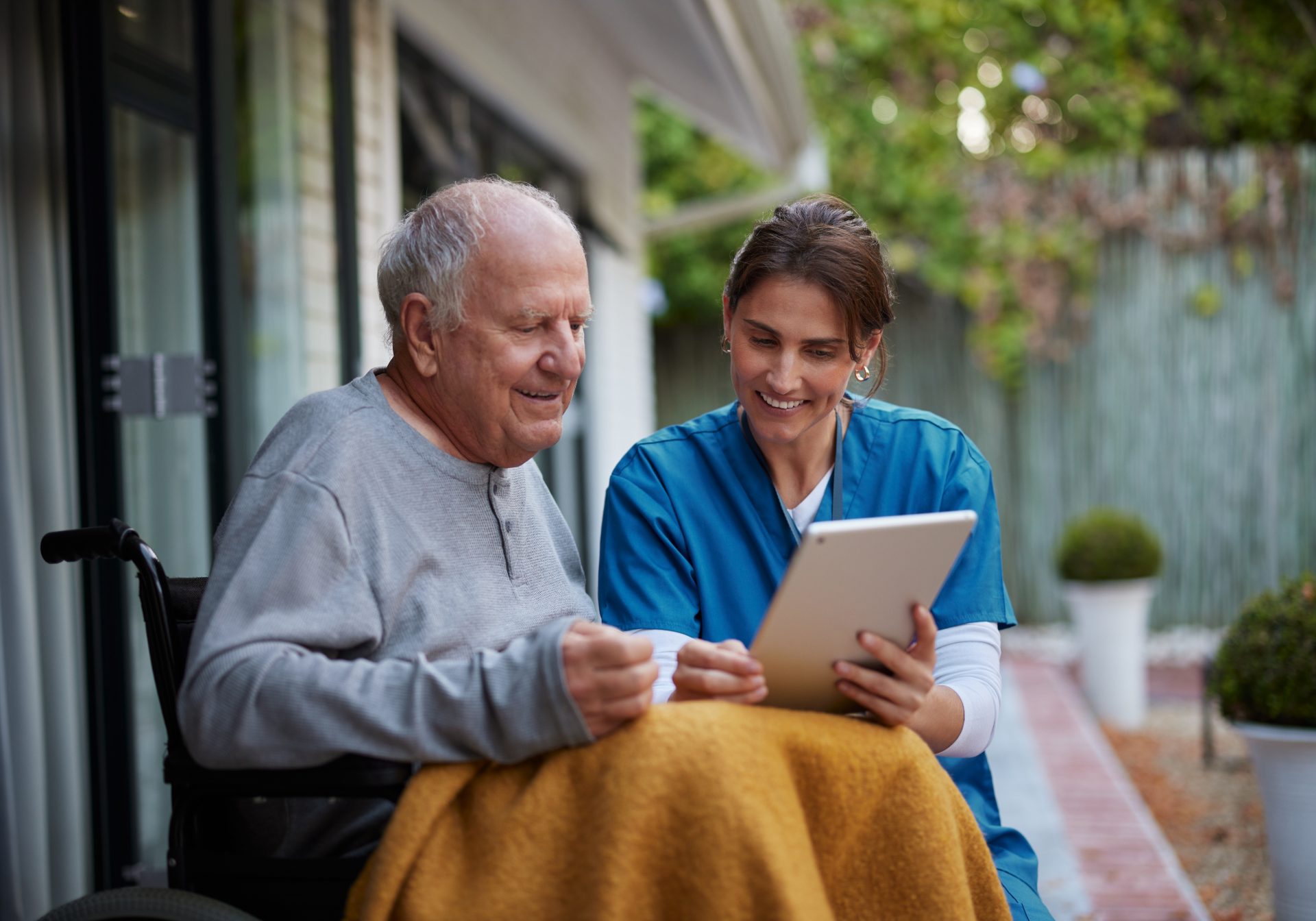 Home care nurse reviewing a tablet with an older man in a wheelchair, the visit home health billing documents
