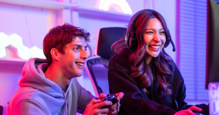 Two players laughing at a neon-lit gaming desk, one in a headset