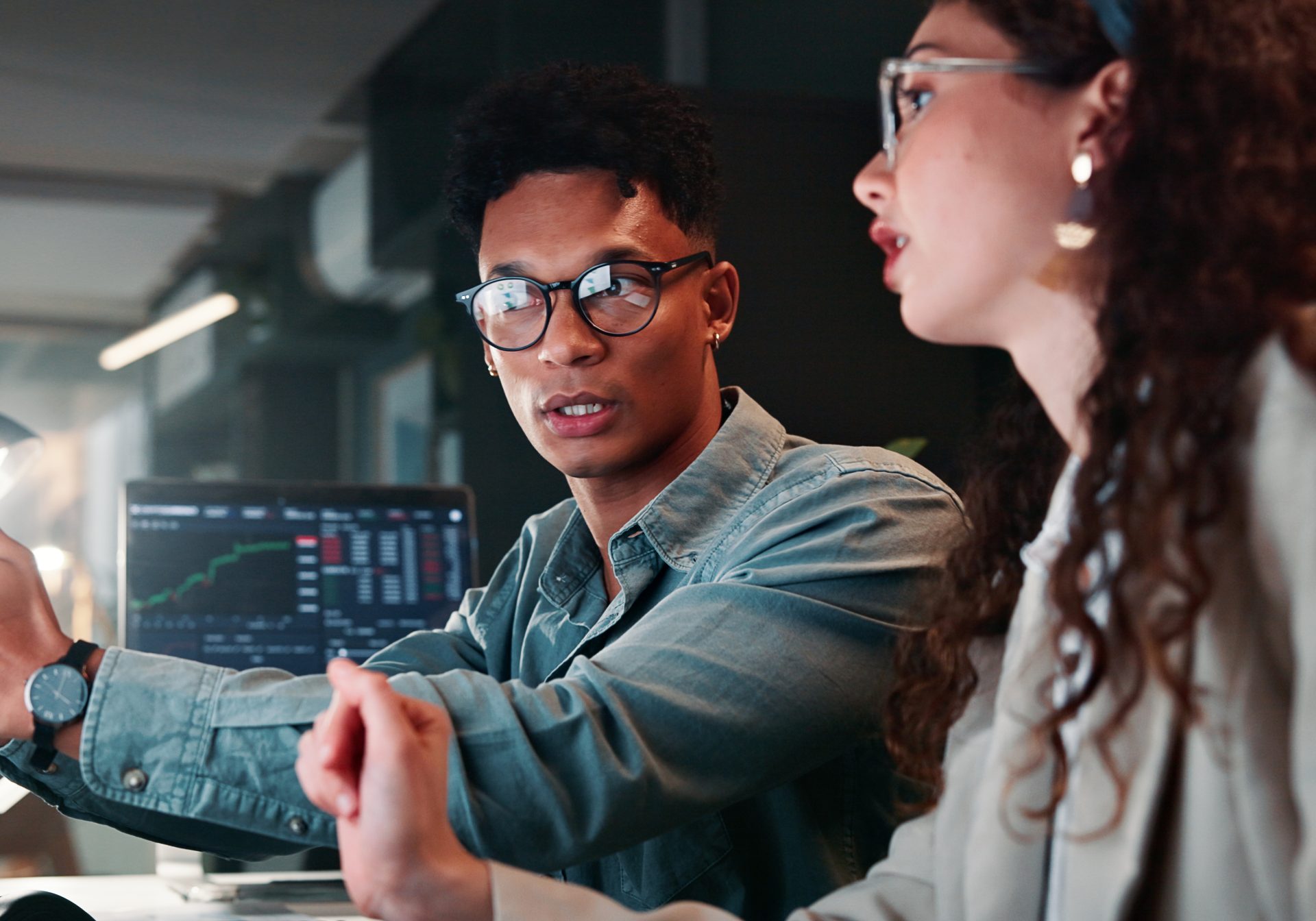 Two colleagues discussing a trading screen at night, working through an investment platform trade query