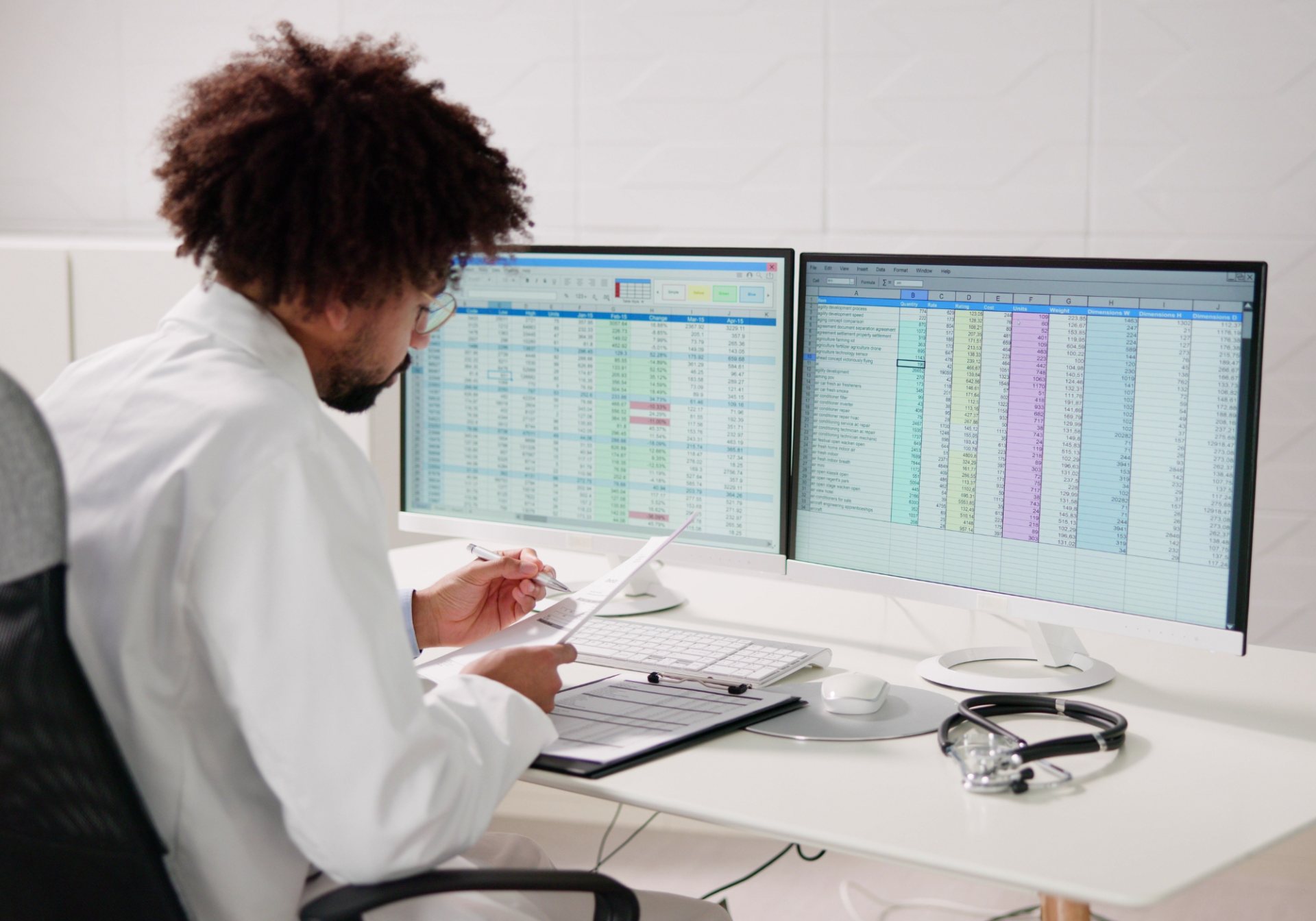 Clinician reviewing billing spreadsheets on two monitors, the claim detail behind laboratory billing