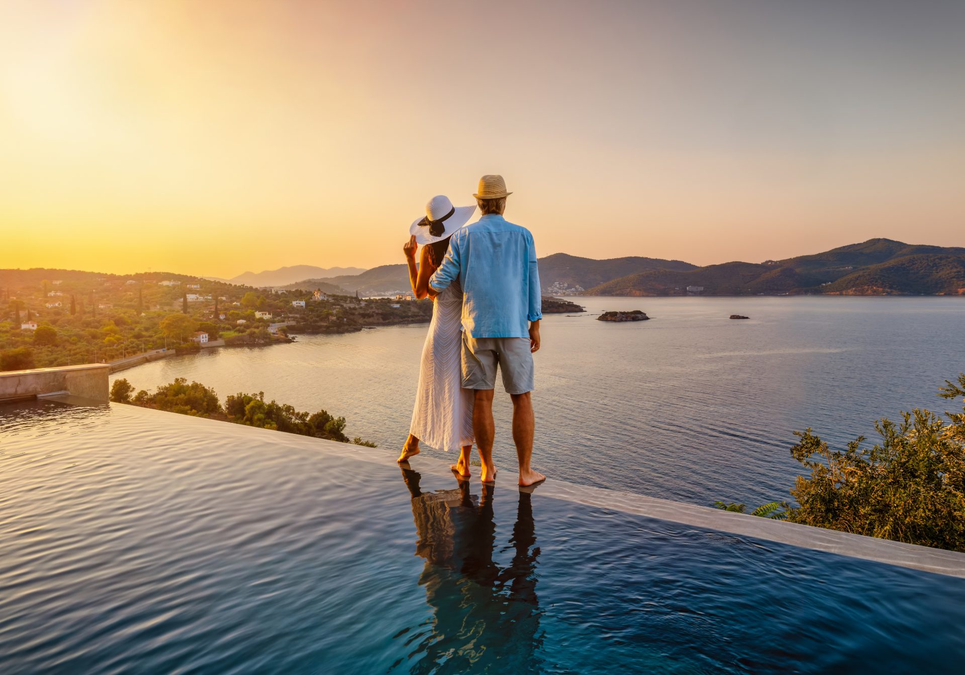 Couple at the edge of an infinity pool above a bay at sunset, the stay a luxury concierge desk arranges