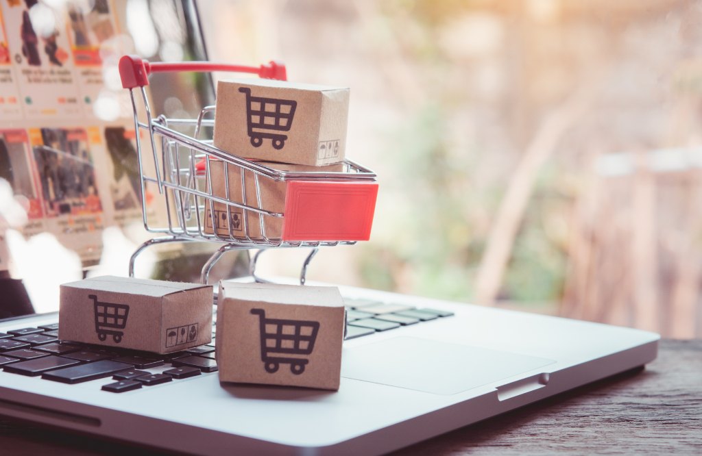 Miniature shopping cart and parcels with cart icons on a laptop keyboard, representing marketplace and catalog management outsourcing to the Philippines