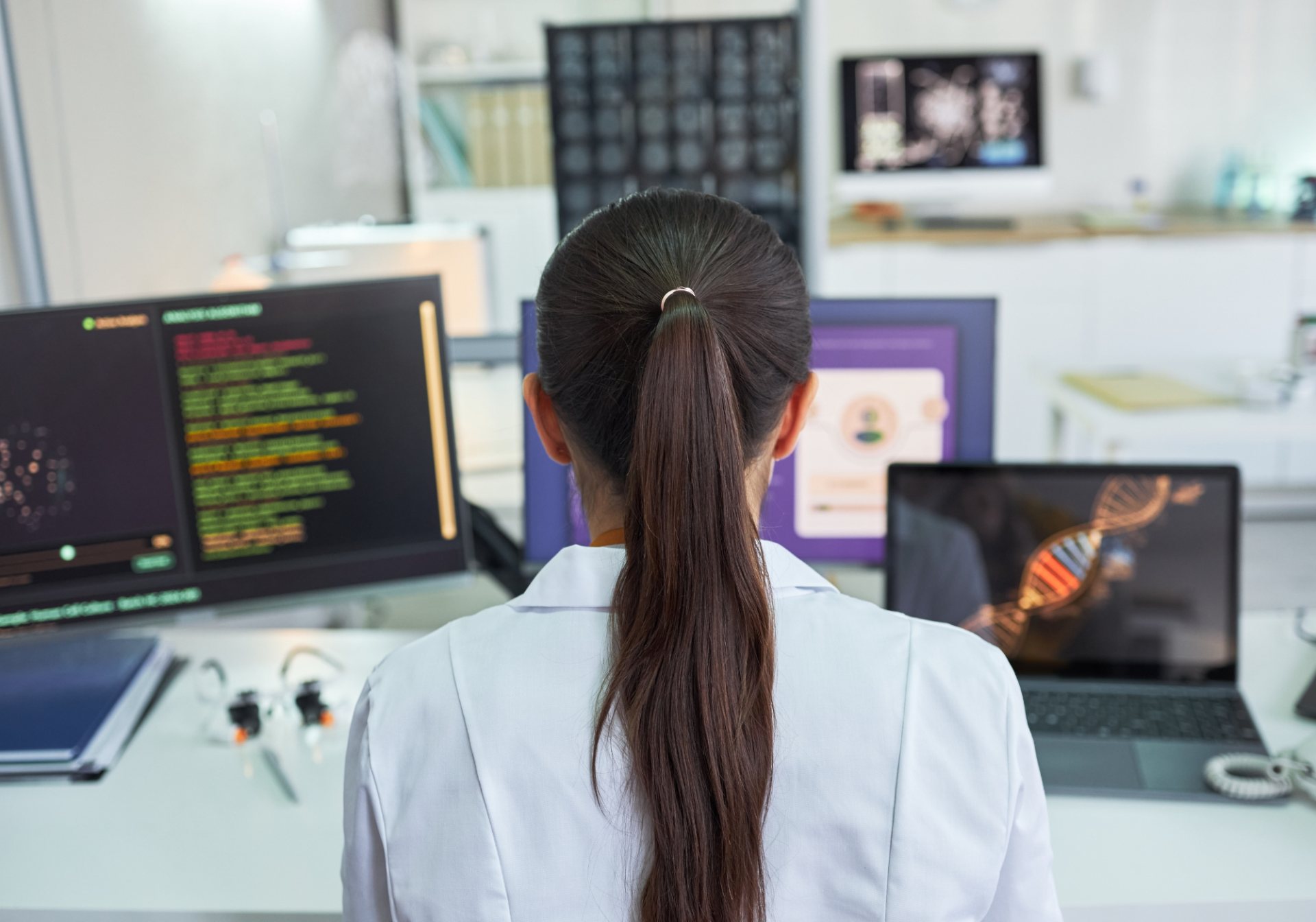 Clinician in a lab coat reviewing medical images and genomic data on several screens for AI labeling