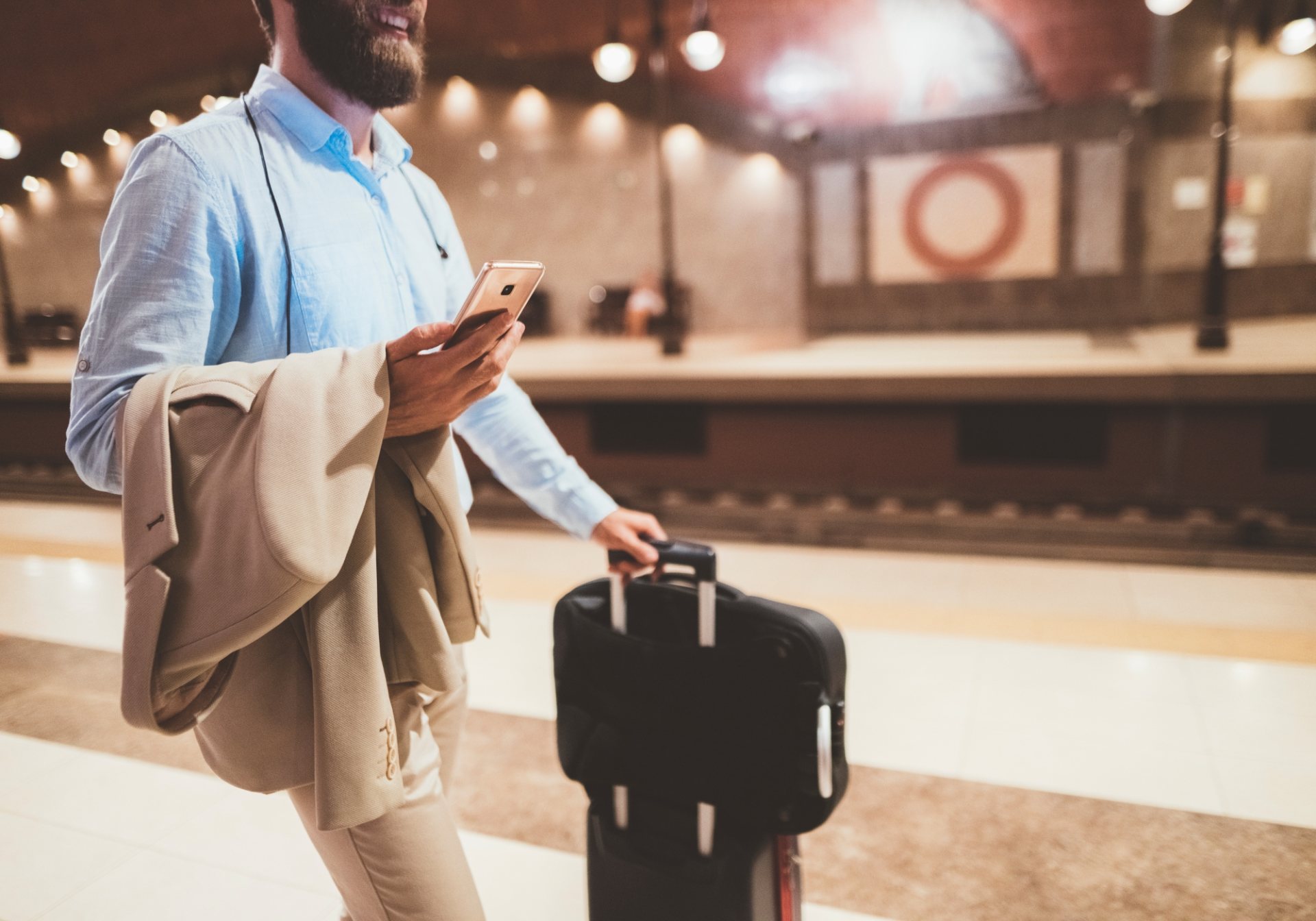 Business traveler with a phone and rolling suitcase on a station platform, for a post on room block attrition
