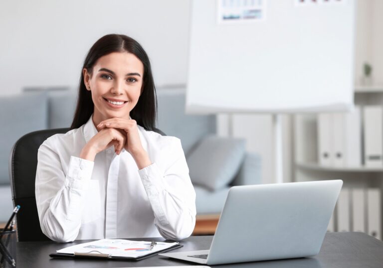 Smiling help desk lead at her desk with a laptop, for a post on help desk identity verification