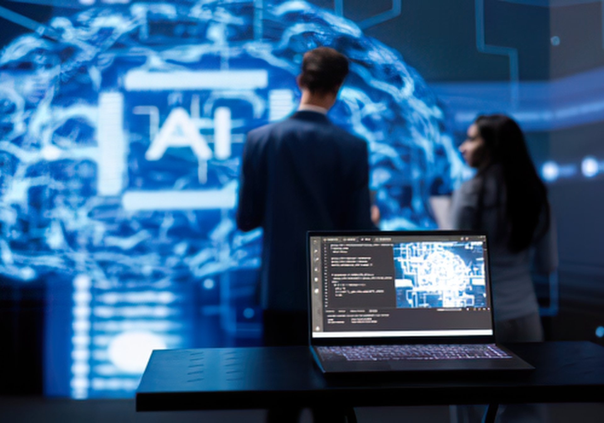 Laptop of code in front of two specialists at an AI display wall, rating image, video and audio outputs