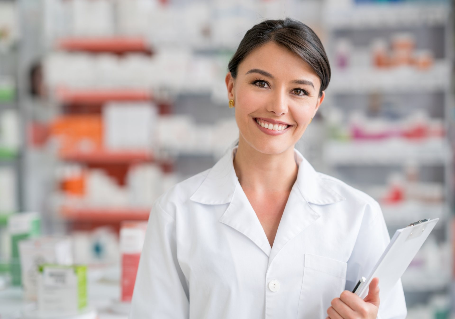 Pharmacist with a clipboard in a pharmacy aisle, where many adverse event reports for pharmacovigilance begin