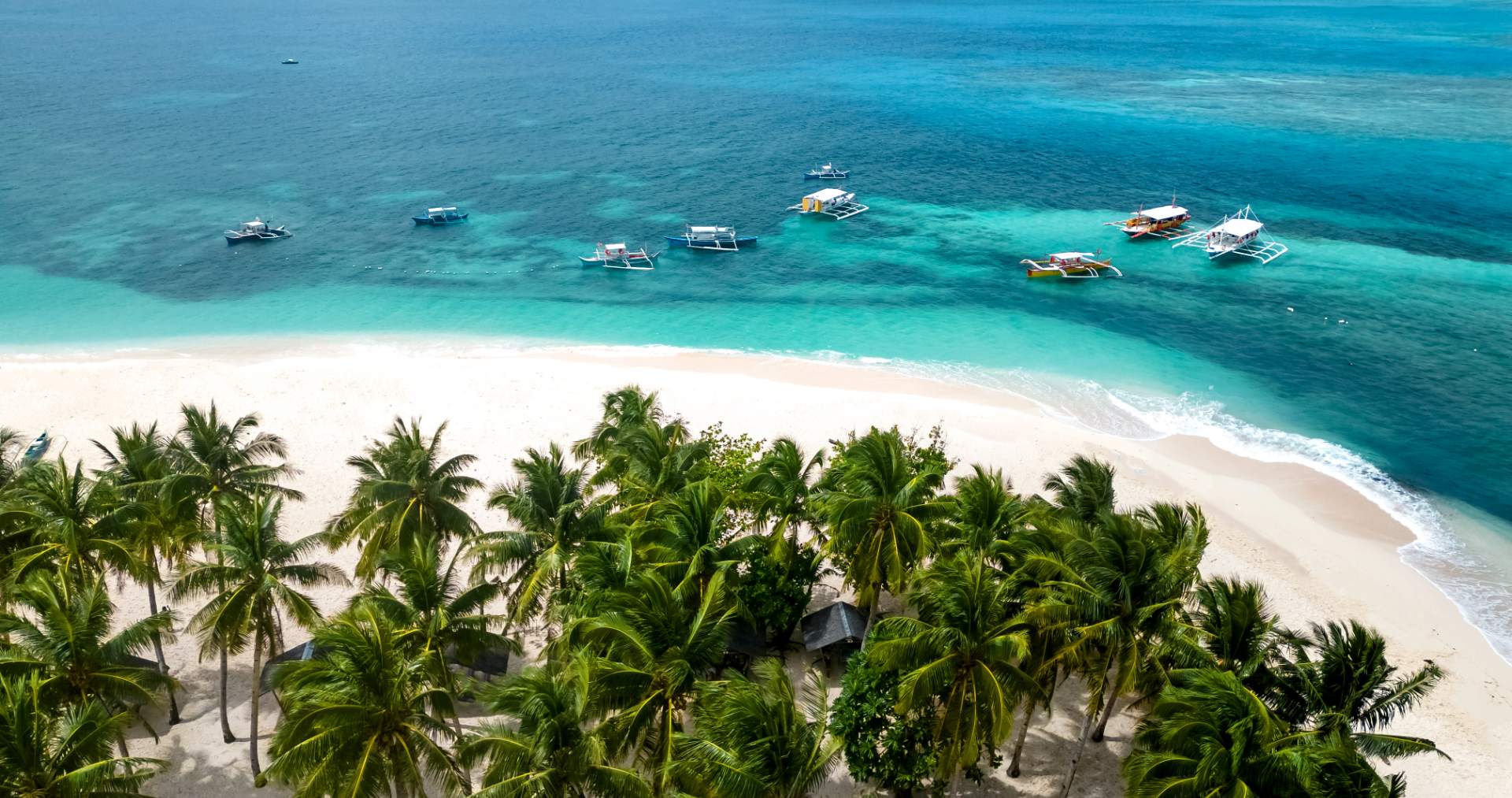 Aerial view of a white-sand Philippine island beach with coconut palms and bangka outrigger boats