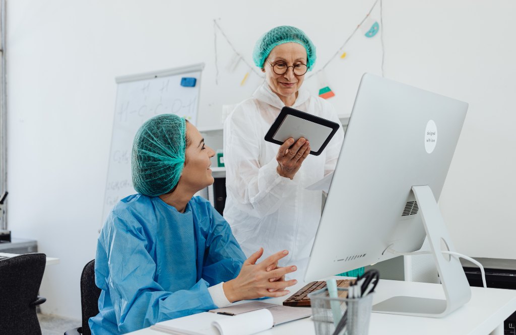 Two clinicians in surgical caps reviewing a case at a computer, representing prior authorization outsourcing from the Philippines