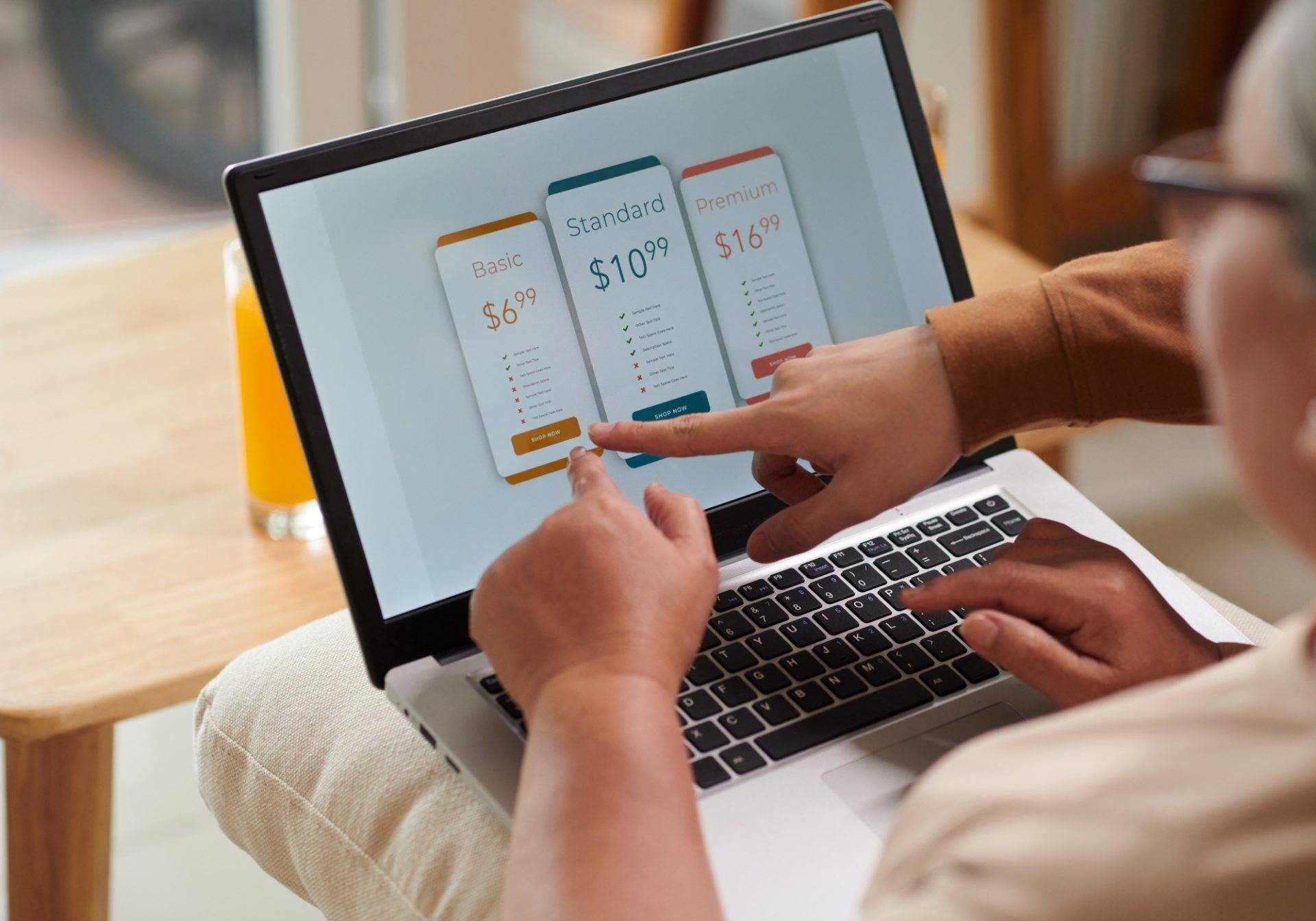 Two people pointing at subscription plan tiers on a laptop, choosing a replenishment plan