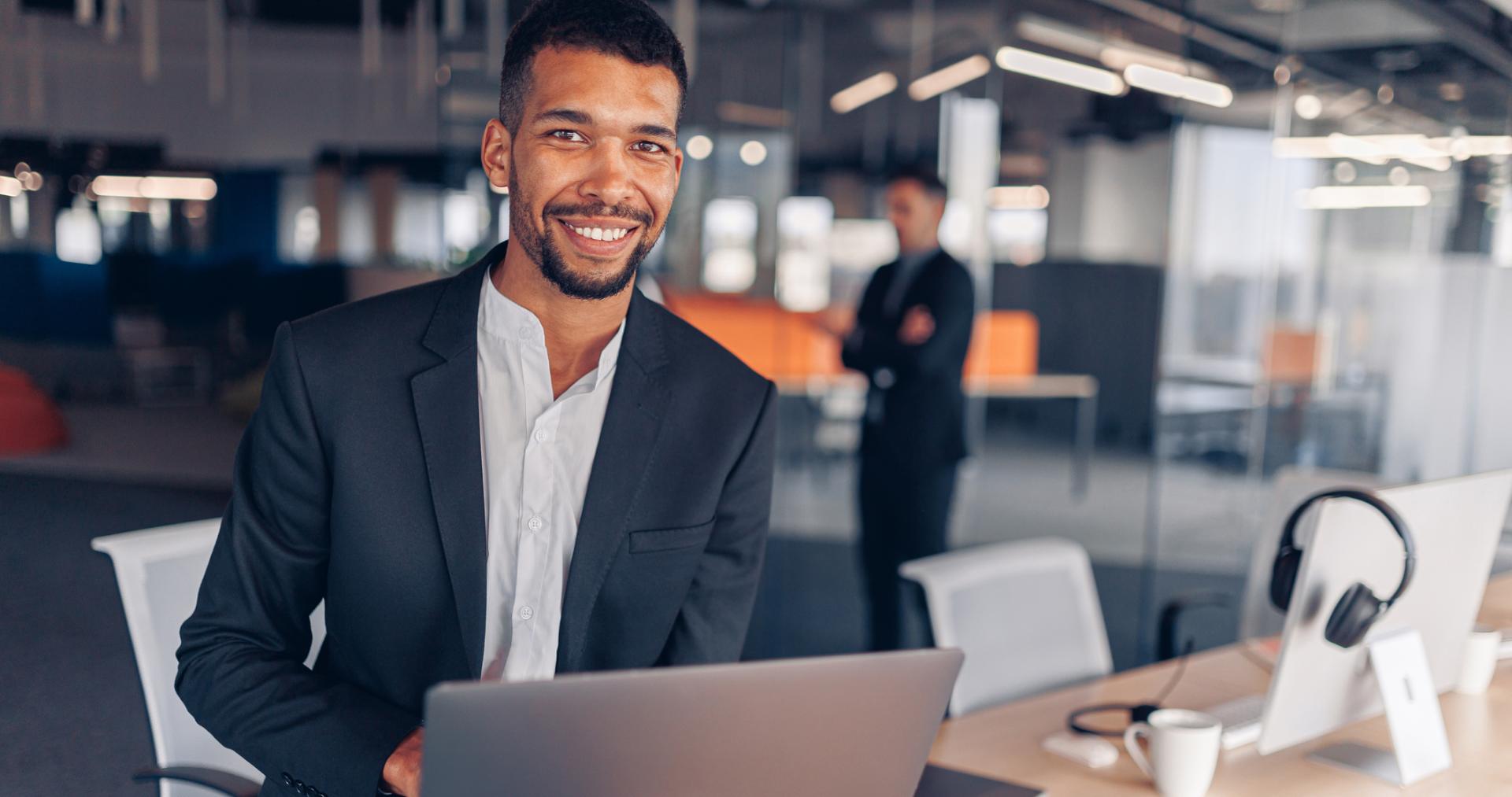 Smiling technology professional holding a laptop in a modern open-plan tech office