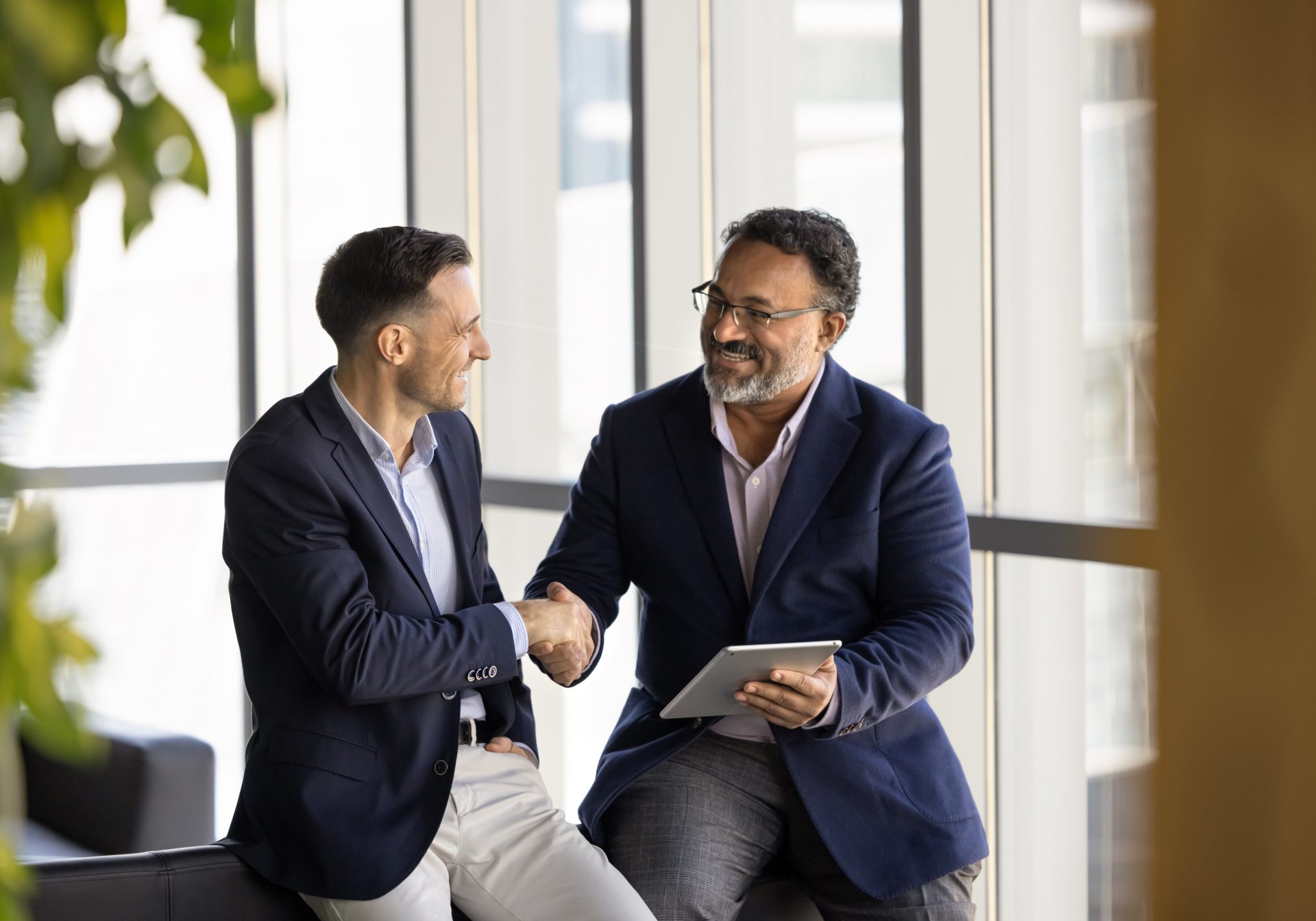 Advisor with a tablet shaking hands with a client by a window, the relationship a wealth service team supports