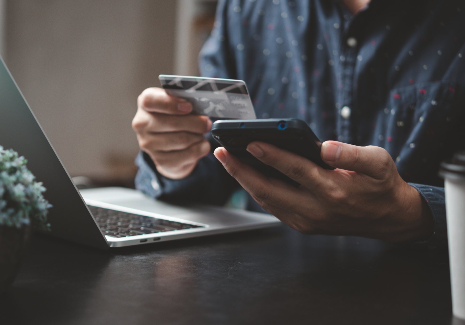 Hands holding a payment card and smartphone beside a laptop, paying inside a WhatsApp chat